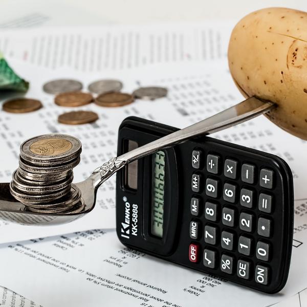 Spoon with a stack of coins in it is balanced on a small calculator with a potato weighing down the other end. 