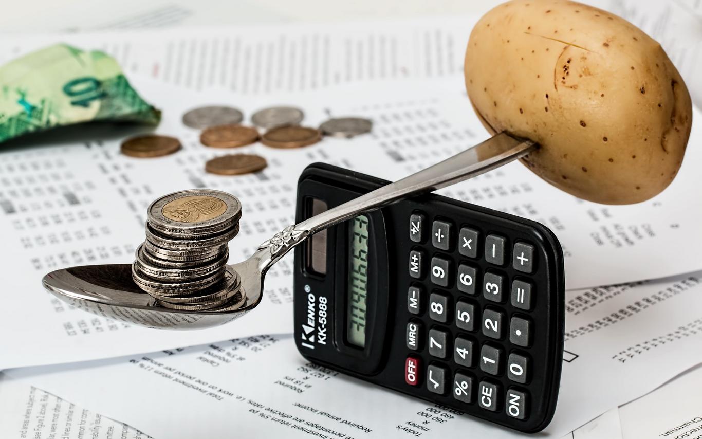 Spoon with a stack of coins in it is balanced on a small calculator with a potato weighing down the other end. 